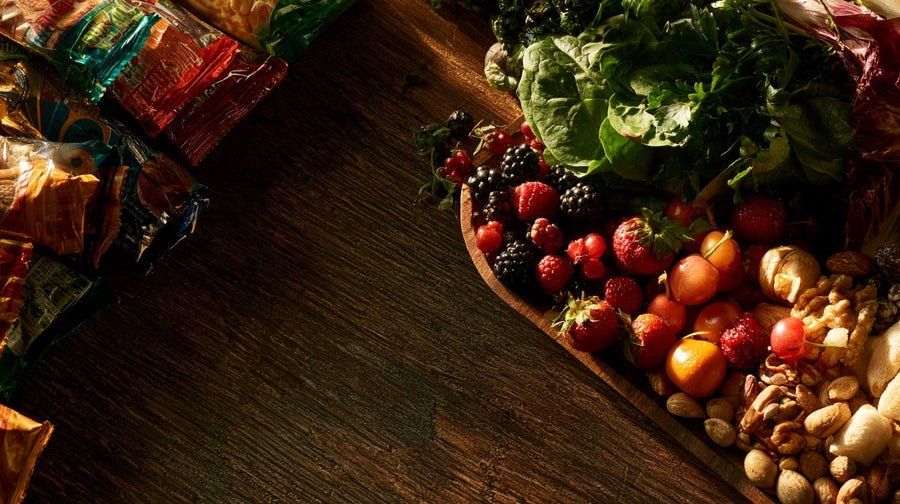 Overhead still life contrasting packaged snacks with fresh whole foods, representing ultra-processed foods and gut health | Gutsi