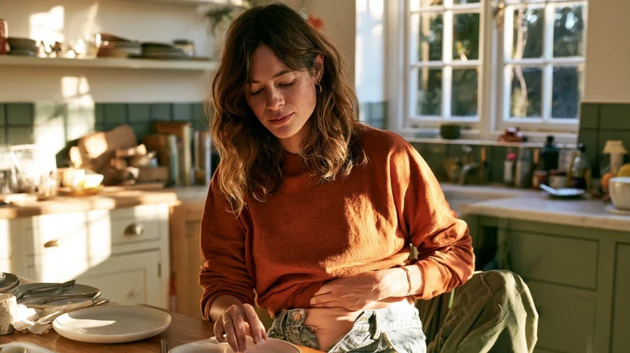 Woman resting a hand on her bloated stomach after lunch, representing SIBO symptoms | Gutsi