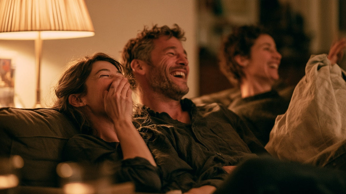 Two friends laughing on a sofa, one wafting a cushion, why do I fart so much | Gutsi
